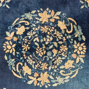 Close-up of a blue rug featuring a circular floral medallion pattern in gold and sage tones.