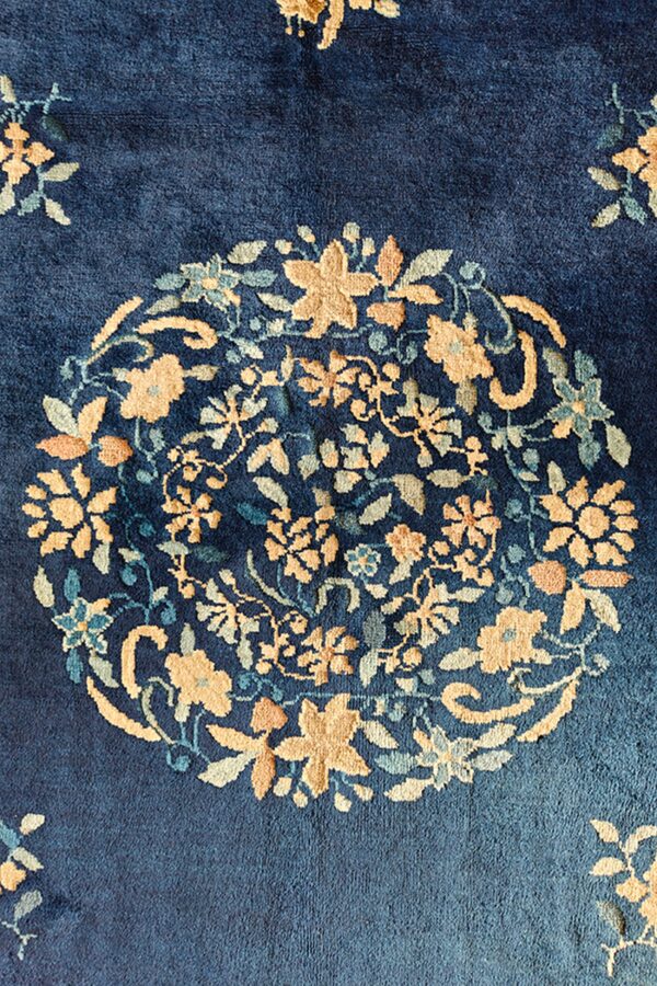 Close-up of a blue rug featuring a circular floral medallion pattern in gold and sage tones.