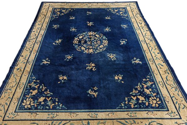 Navy blue rug with a tan border and central floral medallion over a scattered pattern.