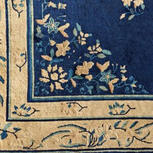 Corner detail of a blue and beige rug with large floral motifs on a deep navy pile background.