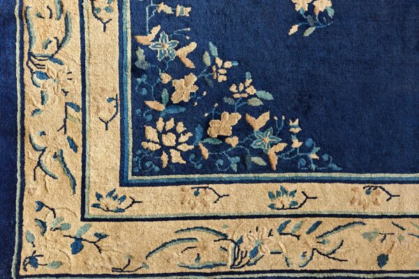 Corner detail of a blue and beige rug with large floral motifs on a deep navy pile background.