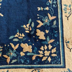 Navy blue rug with tan, teal, and pink floral designs transitioning into a wide beige border.