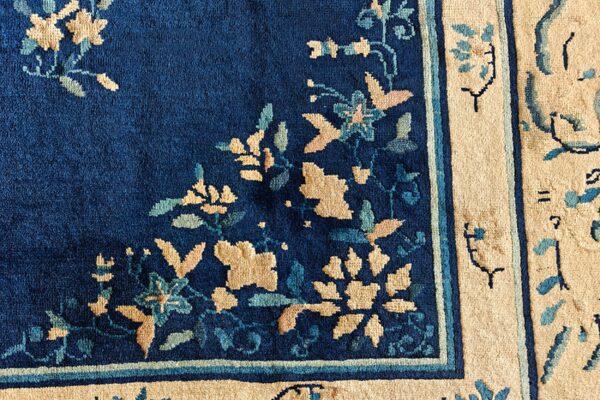 Navy blue rug with tan, teal, and pink floral designs transitioning into a wide beige border.