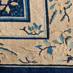 Textured tan rug corner with a thick navy blue border and scattered blue floral and vine patterns.