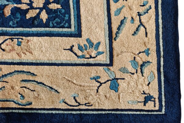 Textured tan rug corner with a thick navy blue border and scattered blue floral and vine patterns.