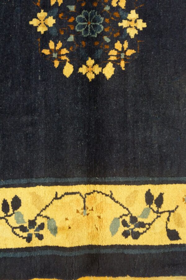 Navy blue rug detail featuring yellow floral patterns and a border with dark blue vine motifs.