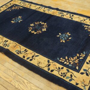 Navy blue rug featuring gold floral borders and scattered motifs rests on light wood plank flooring.