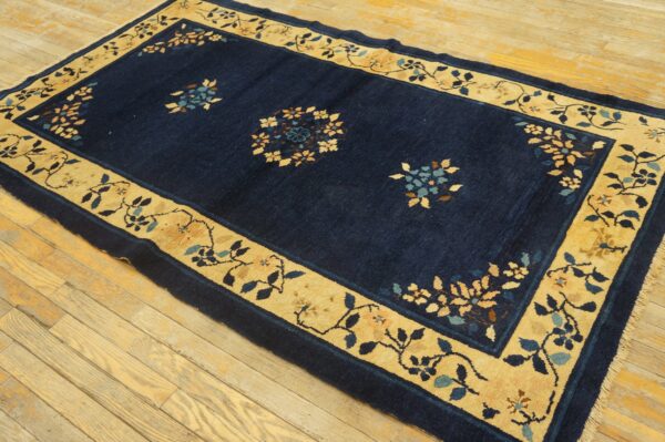 Navy blue rug featuring gold floral borders and scattered motifs rests on light wood plank flooring.
