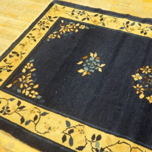 Navy blue rug featuring a golden yellow border with floral vine patterns on wooden planks.