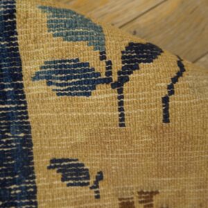 The curved edge of a tan rug with blue floral patterns rests on worn wooden floorboards.