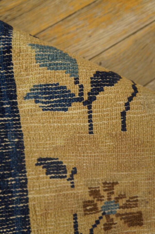 The curved edge of a tan rug with blue floral patterns rests on worn wooden floorboards.