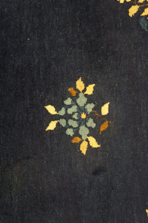 Close-up of dark blue rug pile featuring a floral motif in yellow, teal, and brown.