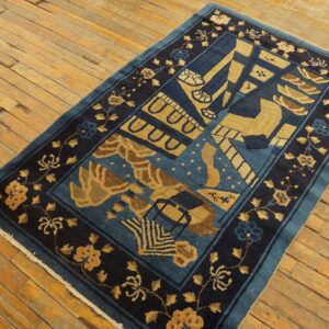 Blue and gold stylized rug with floral borders displayed on worn, yellow-toned wood flooring.