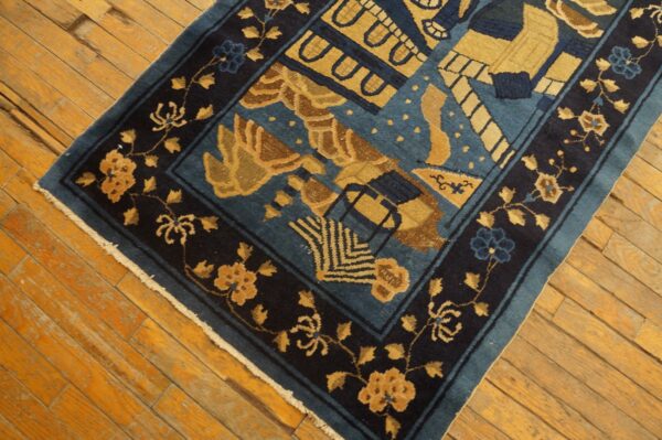 Dark blue rug with tan abstract patterns and a floral border lies on worn wood planks.
