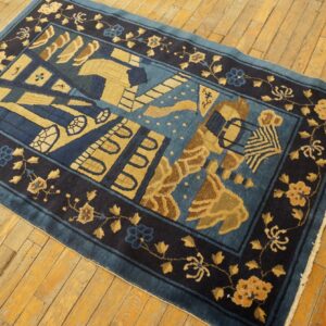 Dark blue rug with a central abstract motif and gold floral borders resting on warm wooden floorboards.