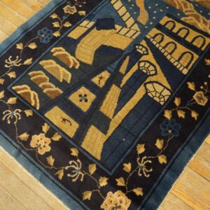 Navy and gold patterned rug with a floral border resting on worn, yellow plank hardwood floors.
