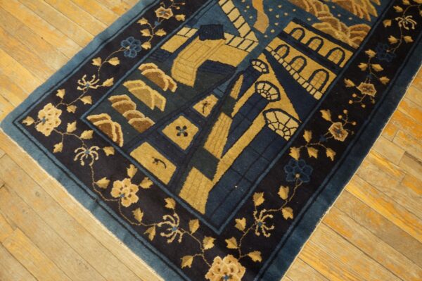 Navy and gold patterned rug with a floral border resting on worn, yellow plank hardwood floors.