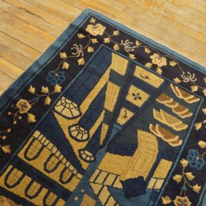 Navy and gold rug featuring abstract central designs and a floral border sits on warm plank wood flooring.