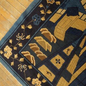 Close up of a navy blue, teal, and gold patterned rug resting on light wood flooring.