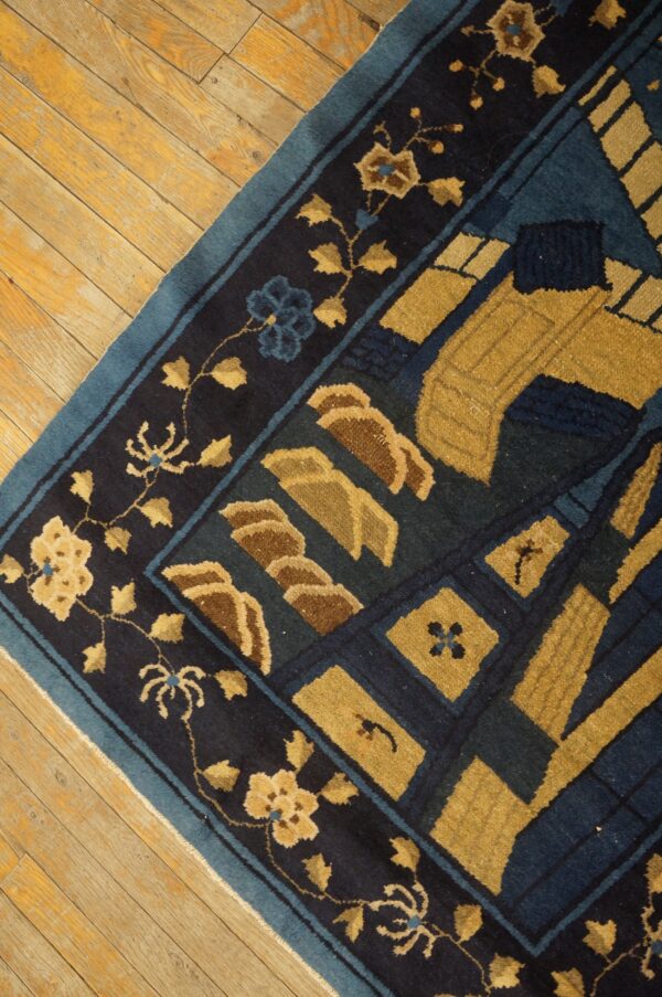 Close up of a navy blue, teal, and gold patterned rug resting on light wood flooring.