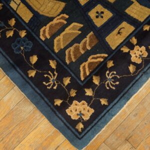 Dark blue rug corner with gold floral and geometric patterns rests on distressed yellow-toned hardwood floors.