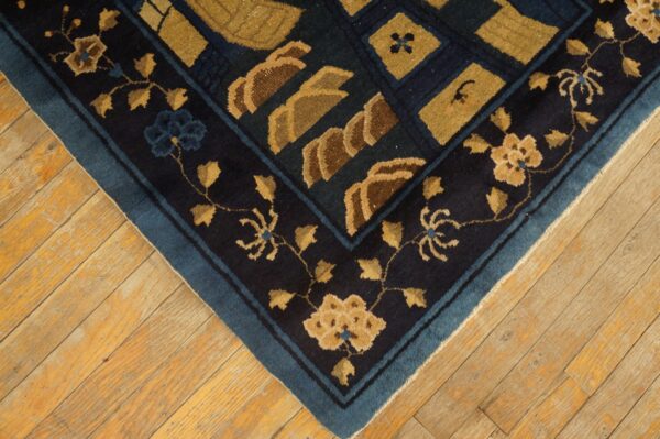 Dark blue rug corner with gold floral and geometric patterns rests on distressed yellow-toned hardwood floors.