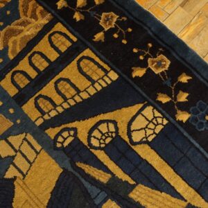Detail of a low-pile rug featuring gold and dark blue architectural designs resting on distressed wood planks.