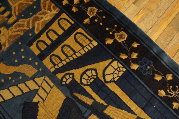 Detail of a low-pile rug featuring gold and dark blue architectural designs resting on distressed wood planks.