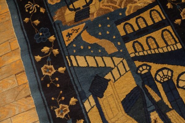 Blue and gold patterned rug displaying stylized buildings and florals next to worn hardwood flooring.