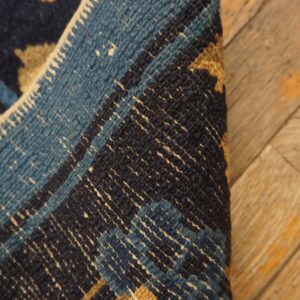 A navy and tan patterned rug is folded over, showing a blue and white woven back and resting on worn wood planks.