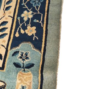 Floral rug detail with navy, beige, and light blue motifs inside thick, muted blue and sage borders.
