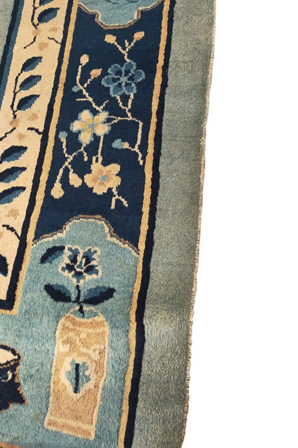 Floral rug detail with navy, beige, and light blue motifs inside thick, muted blue and sage borders.