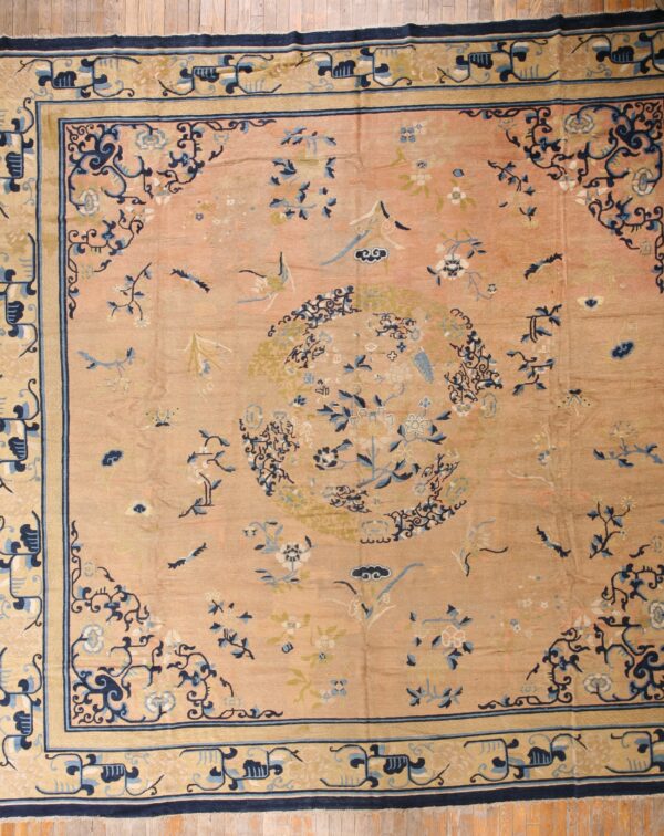Low-pile rug in dusty peach features a navy floral medallion and patterned tan borders on wood flooring.