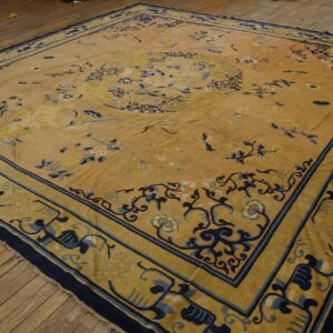 Gold rug with navy and light blue ornate borders and floral motifs, laid on a rustic wood floor.