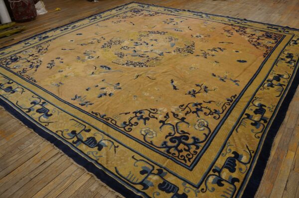 Gold rug with navy and light blue ornate borders and floral motifs, laid on a rustic wood floor.