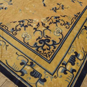 Gold and navy floral rug corner with wide border placed on light brown distressed wood flooring.