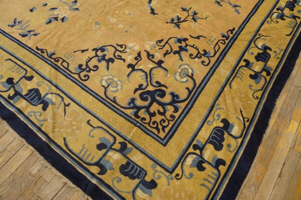 Gold and navy floral rug corner with wide border placed on light brown distressed wood flooring.