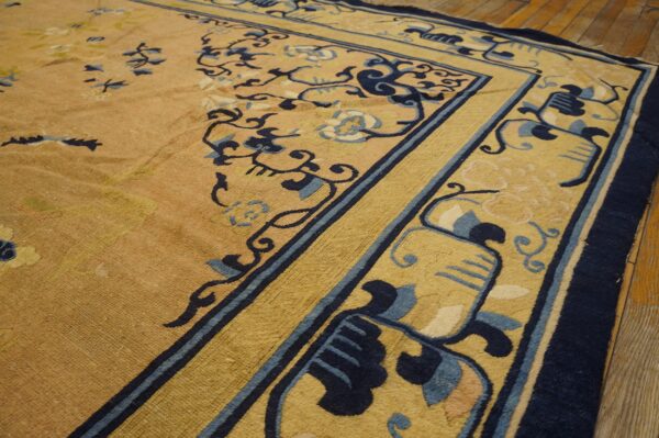 Detail view of a golden yellow rug featuring stylized dark blue vines and floral border motifs on wood flooring.