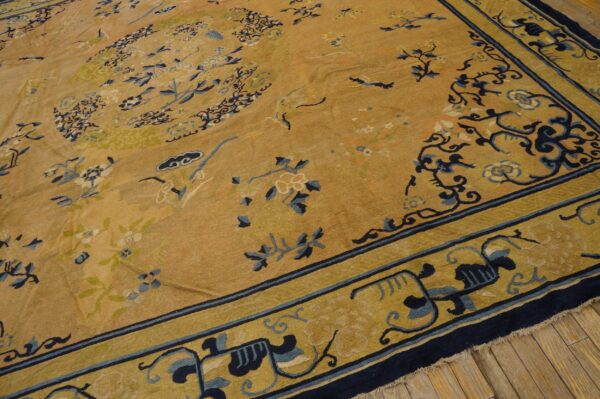 Traditional golden rug with dark blue and pale yellow botanical patterns rests on a wood floor.