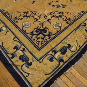 Detail of a gold rug featuring a navy blue and yellow floral corner border on antique wood floors.