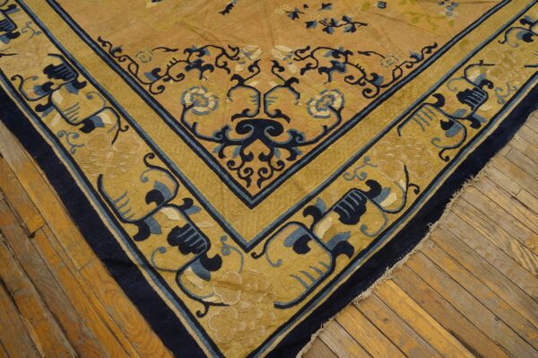 Detail of a gold rug featuring a navy blue and yellow floral corner border on antique wood floors.