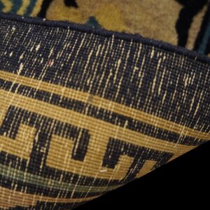 Detail of a rug's backing, revealing a tan and navy geometric meander pattern.