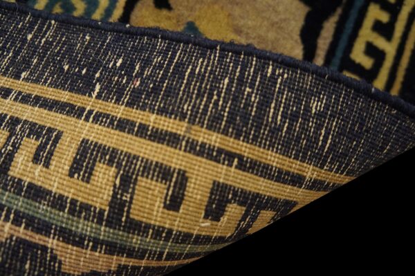 Detail of a rug's backing, revealing a tan and navy geometric meander pattern.