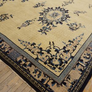 Pale yellow rug with scattered blue floral motifs and a detailed geometric border on light wood planks.