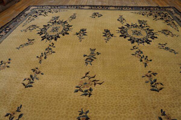 Light gold rug with scattered blue floral motifs and a detailed navy border on wood planks.