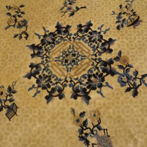 Gold rug detail showing dark blue and black scrolling florals surrounding a geometric central motif.