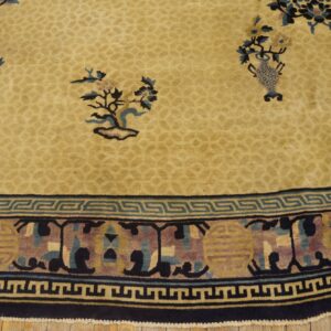 Beige rug with floral details and a dense low-pile texture, bordered by a navy and teal key pattern.