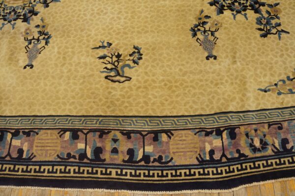 Beige rug with floral details and a dense low-pile texture, bordered by a navy and teal key pattern.