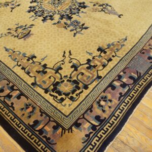Tan rug corner showing ornate dark blue floral and geometric patterns against light yellow plank flooring.