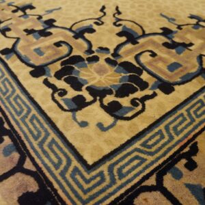 High-pile camel rug detail showing intricate black and blue floral patterns and a geometric key border.